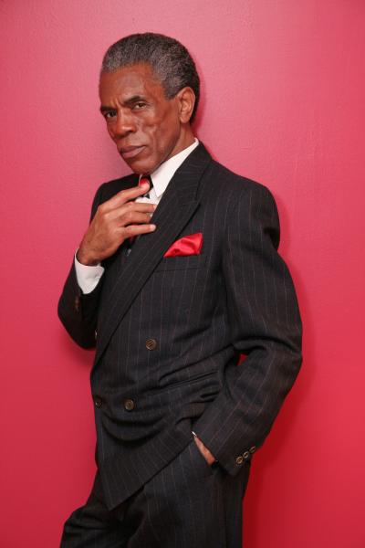 Image of André De Shields in a black suit on a red background